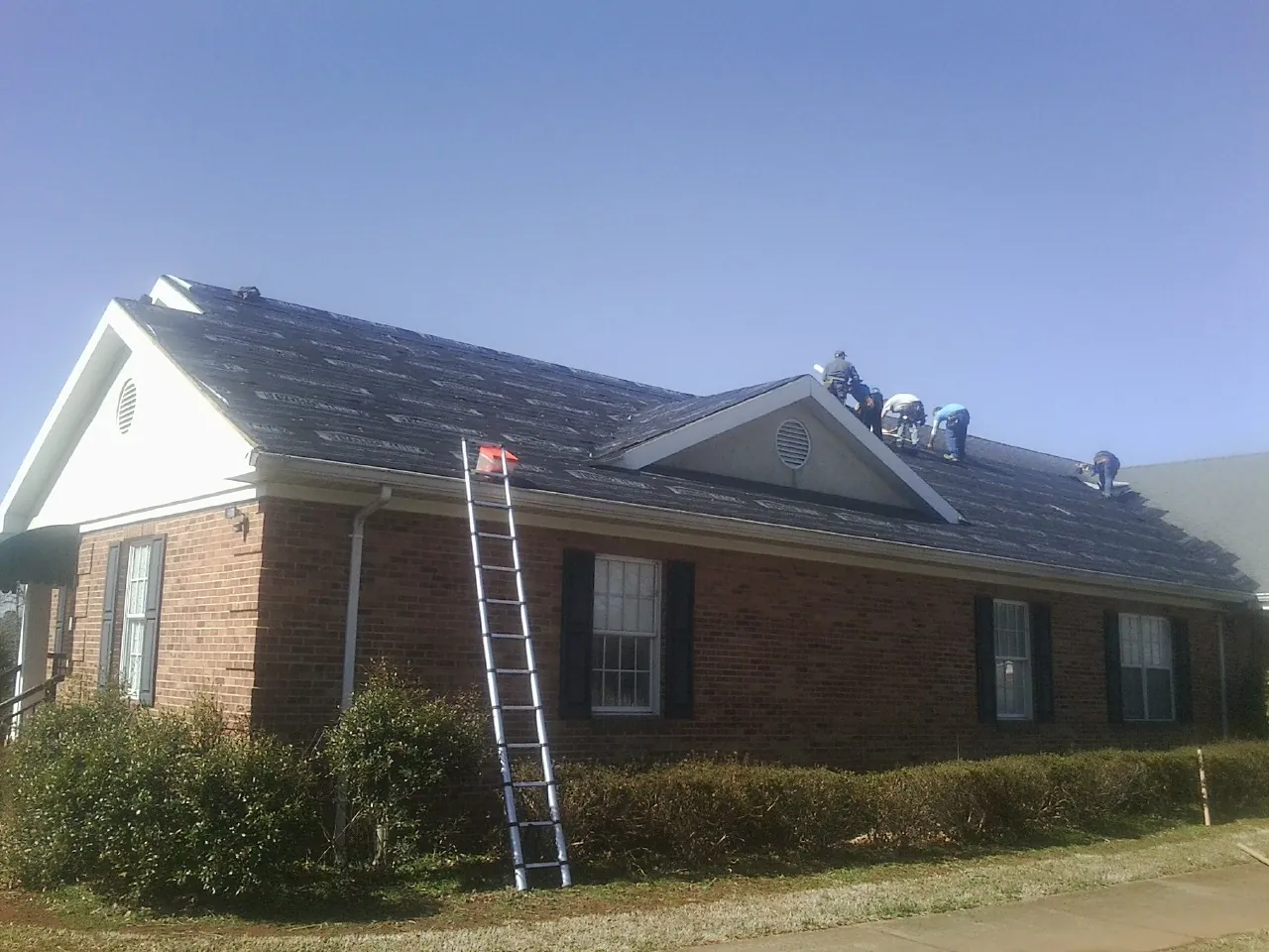 Crew tearing shingles off a brick ranch roof with a ladder set — Metal Roof Repair work by our crew in Sandersville