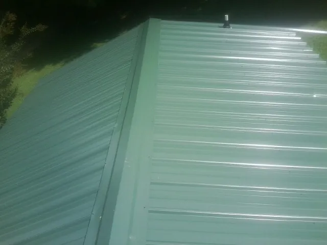 New green metal panels meeting at the ridge of a roof — Flat Roof Repair work by our crew in Sandersville