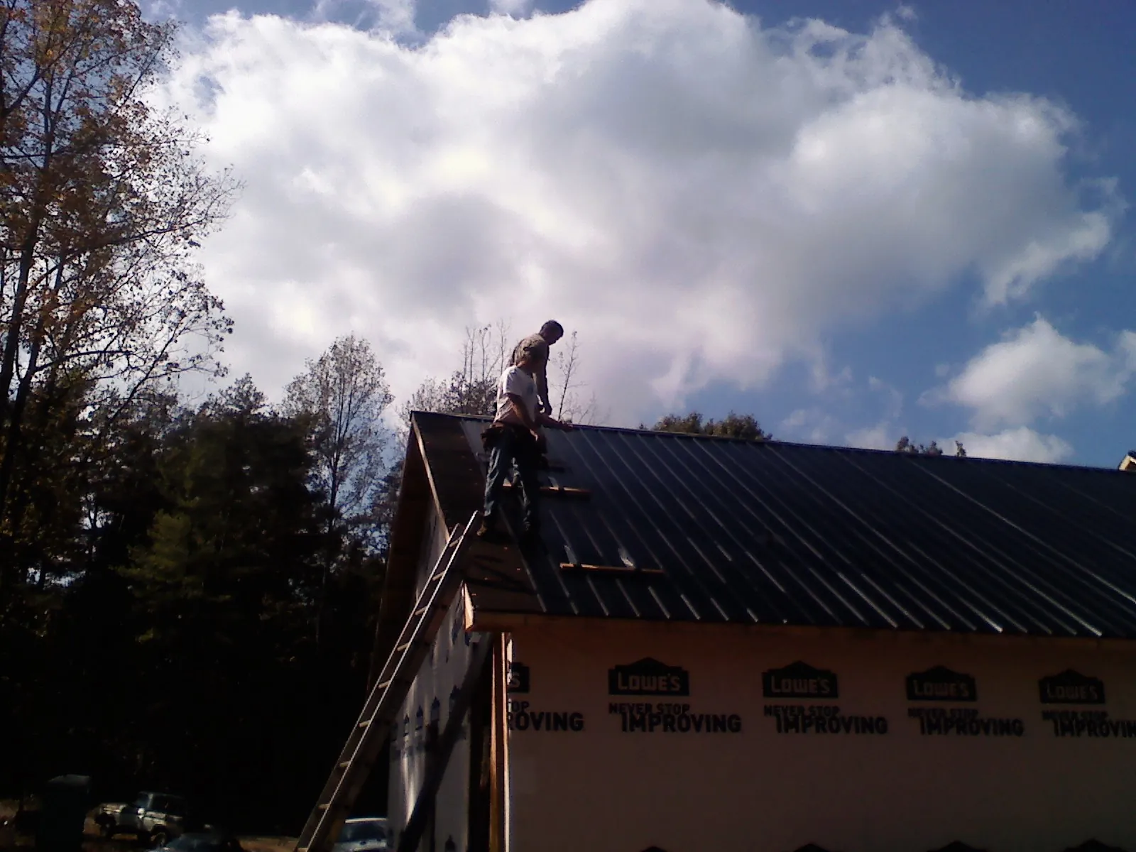 Roofer fastening dark metal panels high against a cloudy sky, from a Roof Inspection job in Sandersville