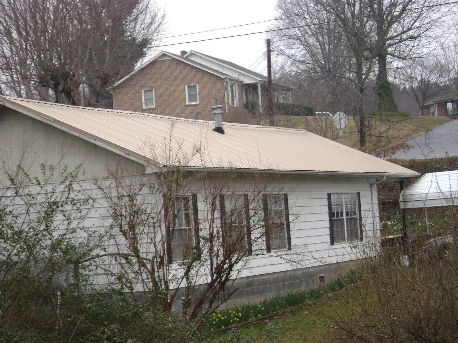 Tan metal roof on a white sided house set into a hillside — Commercial Roofing by Roofing Brothers in Sandersville